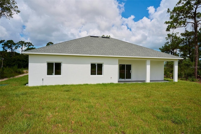 rear view of house featuring a shingled roof, stucco siding, and a lawn