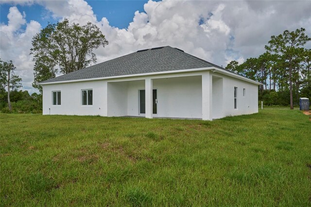back of property featuring a yard, roof with shingles, and stucco siding