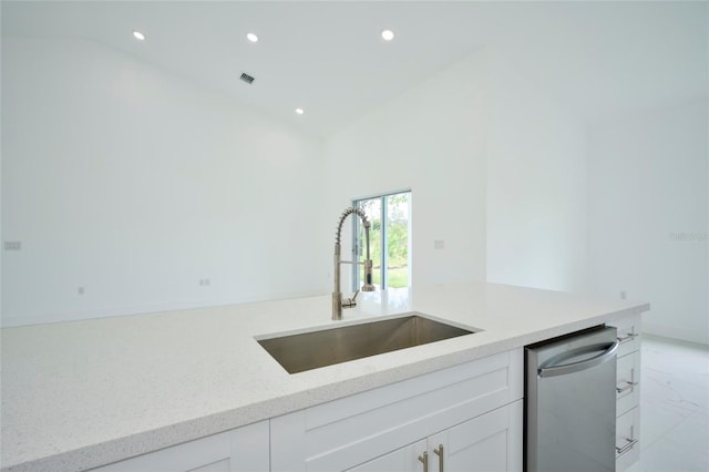 kitchen with light tile patterned flooring, sink, stainless steel dishwasher, and white cabinets