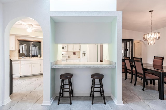 kitchen with white appliances, light tile flooring, ceiling fan with notable chandelier, sink, and white cabinetry