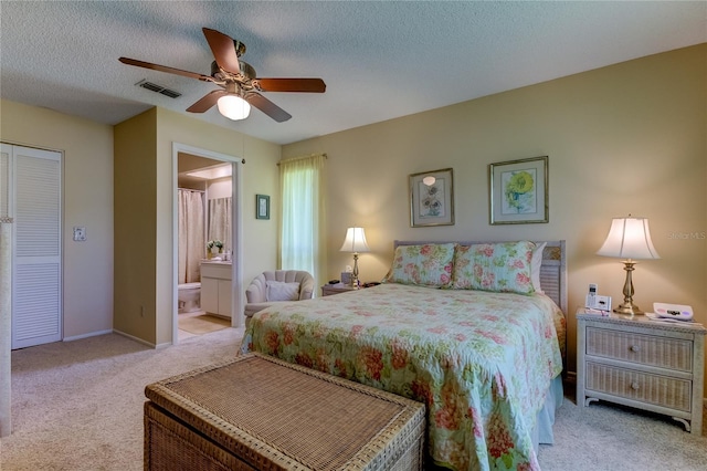 carpeted bedroom with ceiling fan, a closet, a textured ceiling, and ensuite bath