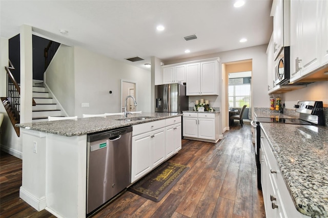 kitchen with dark wood finished floors, a center island with sink, stainless steel appliances, white cabinets, and a sink