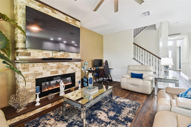 living room featuring baseboards, visible vents, wood finished floors, and a stone fireplace