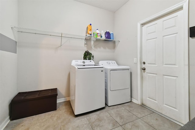 clothes washing area featuring light tile patterned floors, laundry area, independent washer and dryer, and baseboards