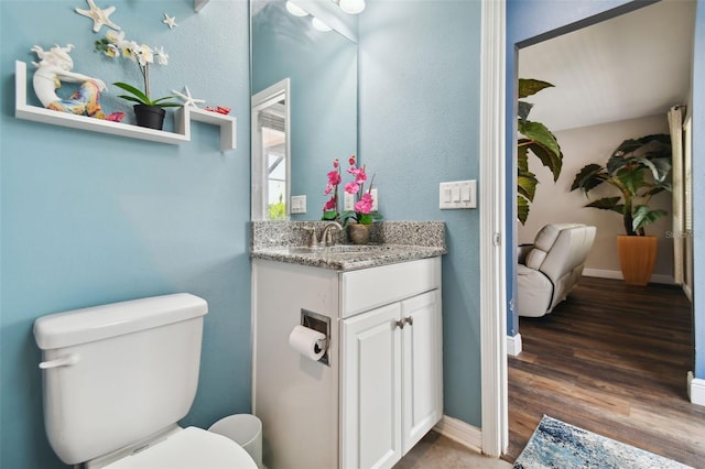 bathroom with baseboards, vanity, toilet, and wood finished floors