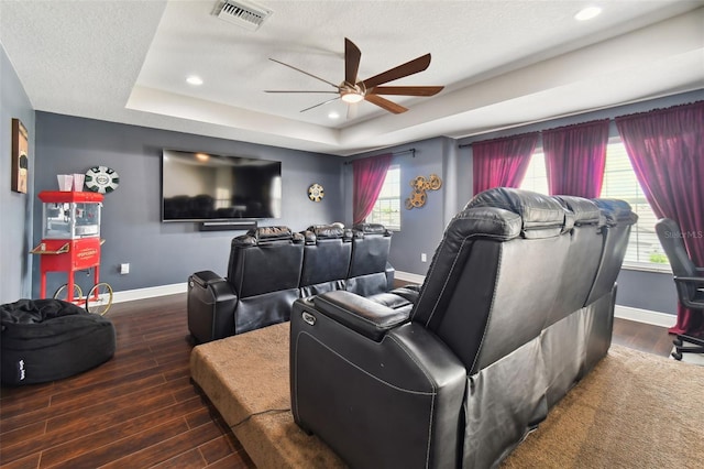 home theater room with a tray ceiling, wood finished floors, and baseboards