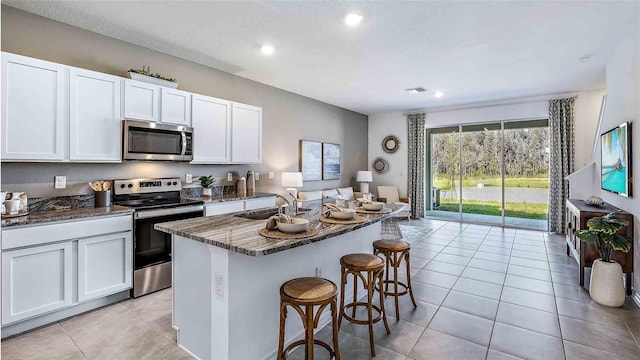 kitchen featuring a breakfast bar area, light tile patterned floors, dark stone counters, a sink, and stainless steel appliances