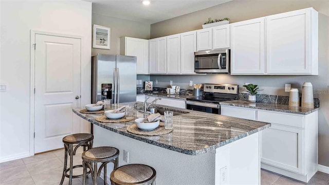 kitchen featuring a kitchen bar, dark stone countertops, appliances with stainless steel finishes, white cabinets, and a sink