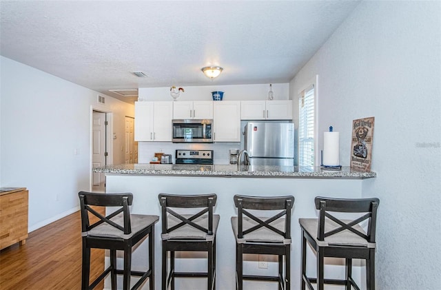 kitchen featuring light stone countertops, backsplash, white cabinetry, and stainless steel appliances