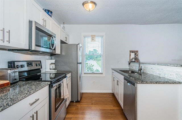 kitchen featuring appliances with stainless steel finishes, a textured ceiling, sink, dark stone countertops, and white cabinetry