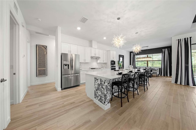 kitchen featuring pendant lighting, a kitchen island with sink, an inviting chandelier, white cabinets, and appliances with stainless steel finishes