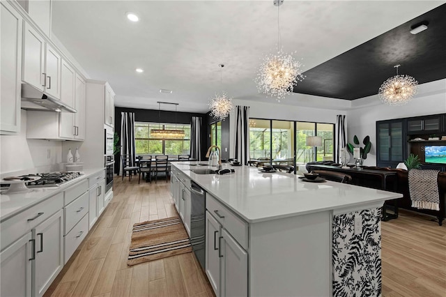 kitchen with a kitchen island with sink, pendant lighting, an inviting chandelier, light hardwood / wood-style flooring, and white cabinetry