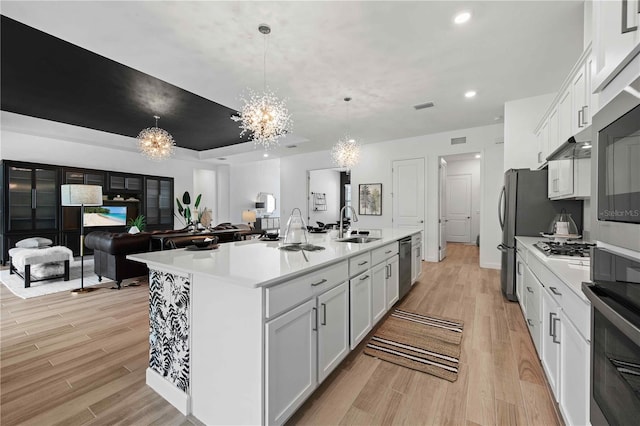 kitchen with stainless steel appliances, pendant lighting, a chandelier, a center island with sink, and white cabinets