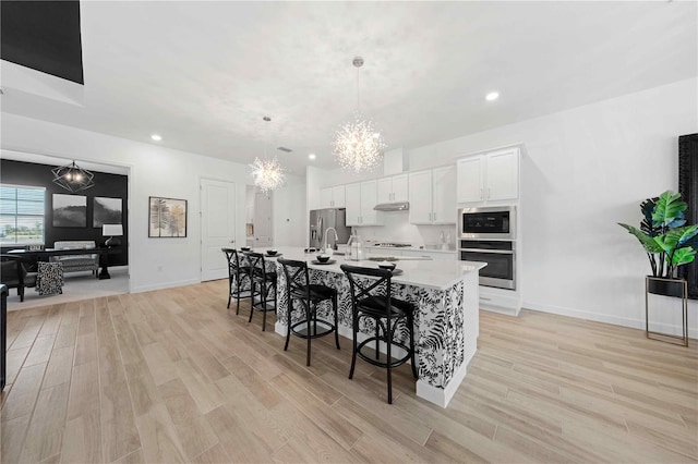 kitchen featuring pendant lighting, a breakfast bar, white cabinets, a center island with sink, and appliances with stainless steel finishes