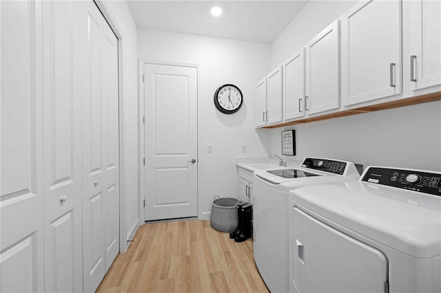 laundry room featuring washer and dryer, light hardwood / wood-style floors, and cabinets