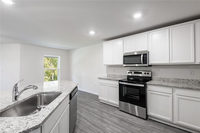 kitchen with white cabinets, stainless steel appliances, light stone counters, and sink