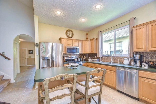 kitchen with sink, backsplash, a textured ceiling, light tile patterned floors, and appliances with stainless steel finishes