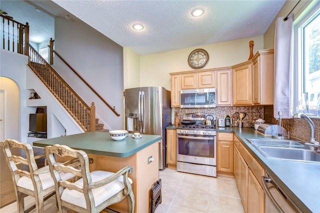 kitchen featuring a breakfast bar, sink, stainless steel appliances, light brown cabinetry, and light tile patterned floors