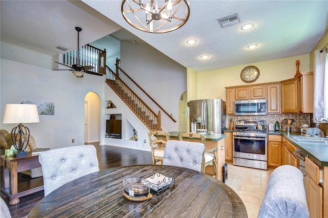 dining space featuring a textured ceiling, sink, light tile patterned floors, and ceiling fan with notable chandelier