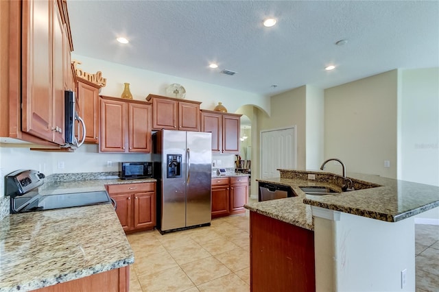 kitchen featuring sink, a textured ceiling, an island with sink, appliances with stainless steel finishes, and stone countertops