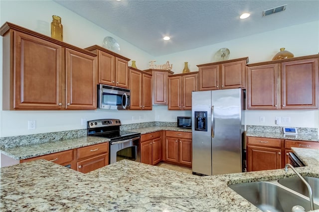 kitchen with light stone countertops, a textured ceiling, stainless steel appliances, and sink