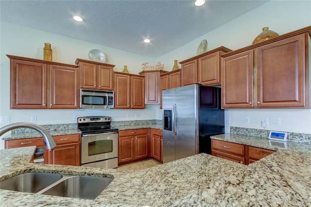 kitchen featuring a textured ceiling, stainless steel appliances, light stone counters, and sink