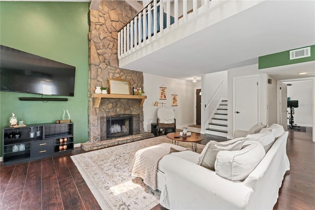 living room featuring a towering ceiling, a stone fireplace, and dark hardwood / wood-style flooring