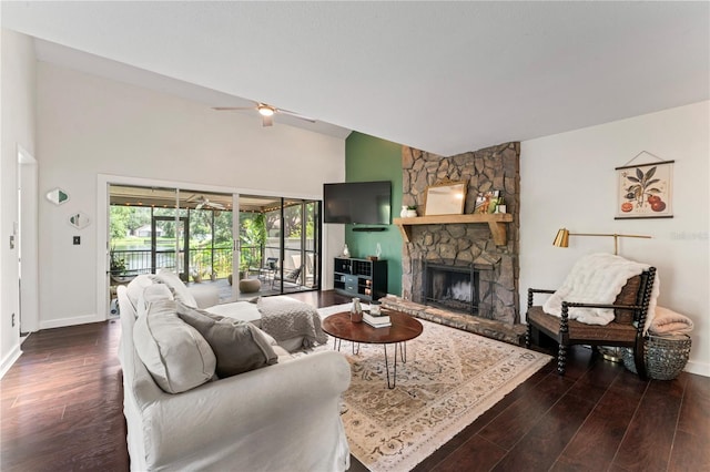 living room featuring ceiling fan, dark hardwood / wood-style flooring, and a stone fireplace