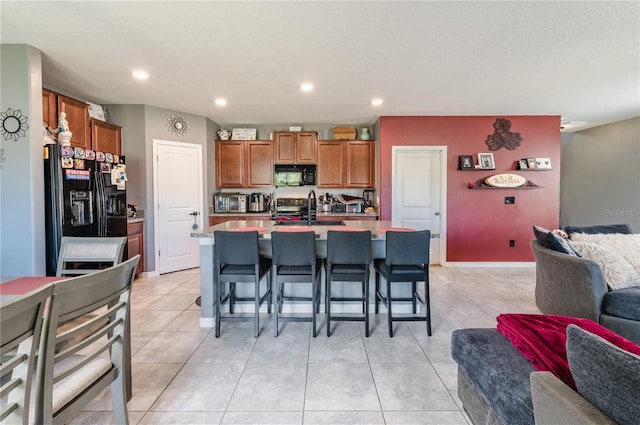 kitchen featuring a kitchen island with sink, light tile patterned floors, a kitchen breakfast bar, and black appliances