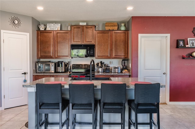 kitchen with sink, light tile patterned floors, black appliances, an island with sink, and a kitchen bar