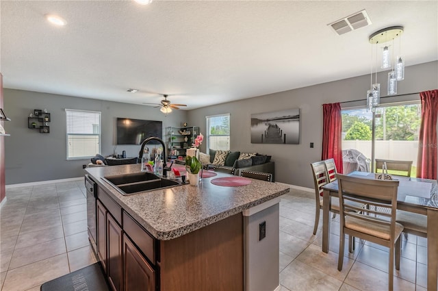 kitchen with light tile patterned flooring, pendant lighting, sink, a kitchen island with sink, and a textured ceiling