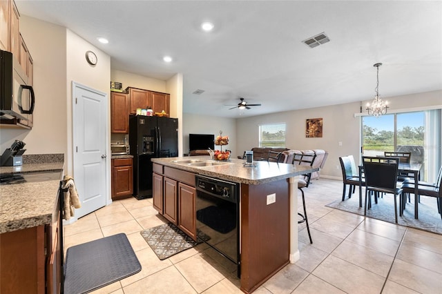 kitchen featuring an island with sink, decorative light fixtures, black appliances, ceiling fan with notable chandelier, and a breakfast bar