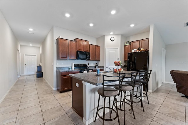 kitchen with light tile floors, a center island with sink, black appliances, and a breakfast bar