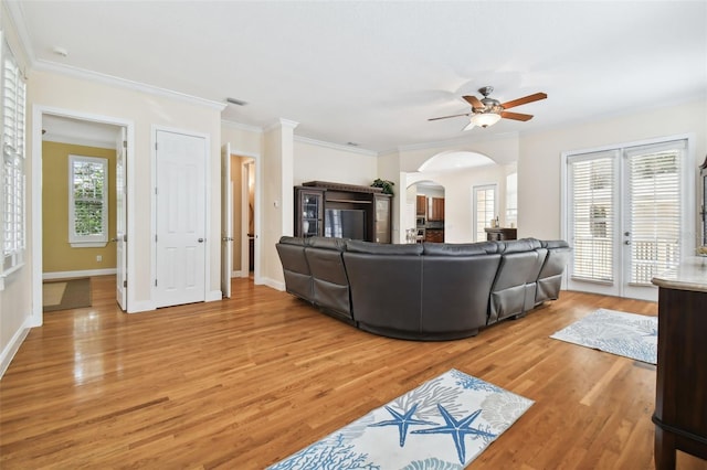 living area featuring arched walkways, light wood-type flooring, a ceiling fan, and baseboards