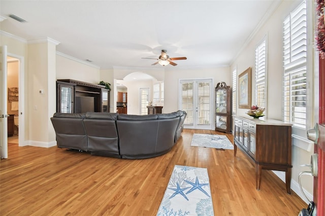 living area featuring arched walkways, visible vents, light wood-style floors, ornamental molding, and baseboards