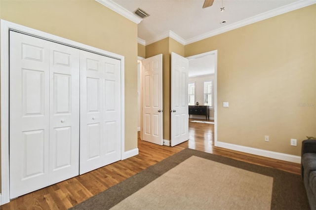 unfurnished bedroom featuring crown molding, a closet, visible vents, wood finished floors, and baseboards