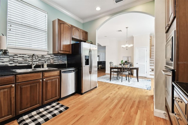 kitchen with stainless steel appliances, a sink, ornamental molding, decorative backsplash, and dark countertops