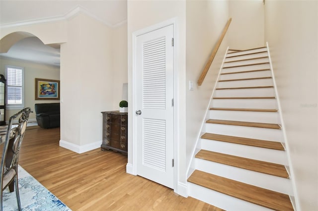 stairs featuring arched walkways, baseboards, wood finished floors, and crown molding