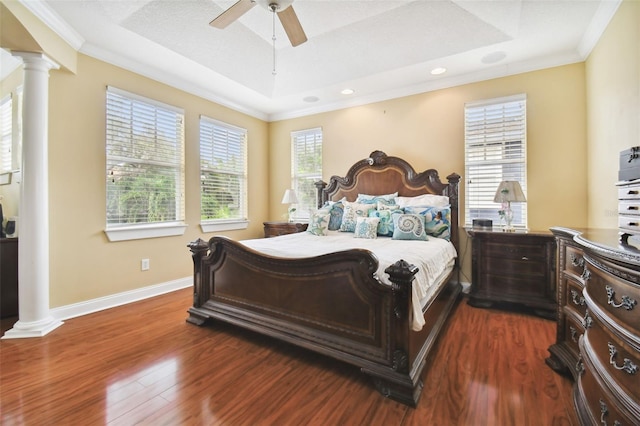 bedroom with decorative columns, ornamental molding, a raised ceiling, and dark wood finished floors