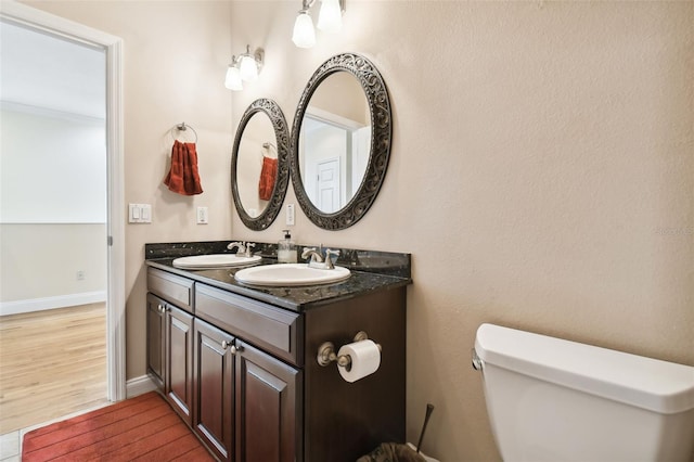 bathroom with toilet, a sink, double vanity, and wood finished floors