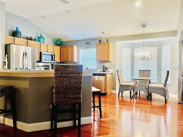 kitchen featuring stainless steel appliances, vaulted ceiling, decorative light fixtures, a notable chandelier, and light hardwood / wood-style floors