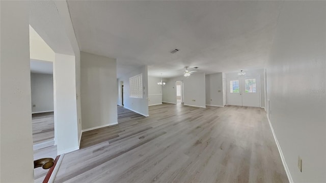 unfurnished living room with ceiling fan with notable chandelier, visible vents, light wood finished floors, and baseboards