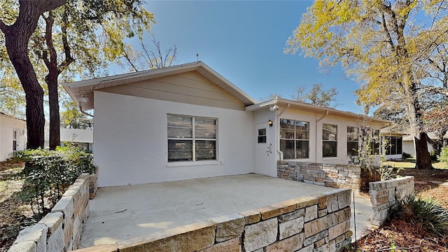 rear view of property featuring a patio, stone siding, and stucco siding