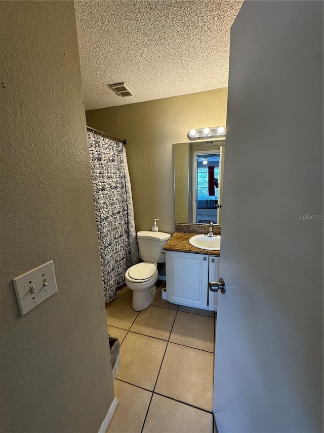 bathroom with tile flooring, large vanity, toilet, and a textured ceiling