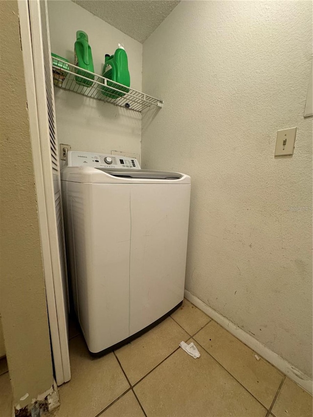 clothes washing area featuring a textured ceiling, light tile flooring, and washer / clothes dryer