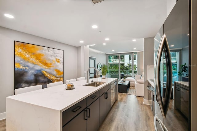 kitchen with sink, dishwasher, a center island with sink, and light wood-type flooring