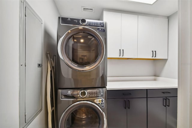 clothes washing area featuring stacked washing maching and dryer and cabinets