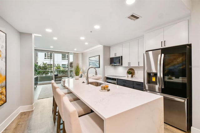 kitchen featuring light hardwood / wood-style flooring, sink, a center island with sink, white cabinets, and stainless steel fridge