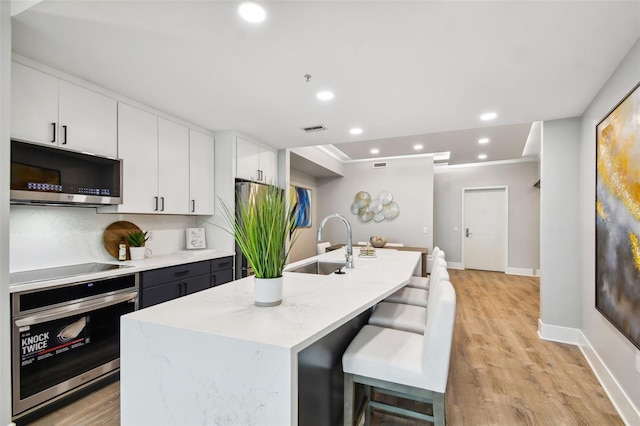 kitchen with appliances with stainless steel finishes, light hardwood / wood-style flooring, white cabinets, and light stone counters