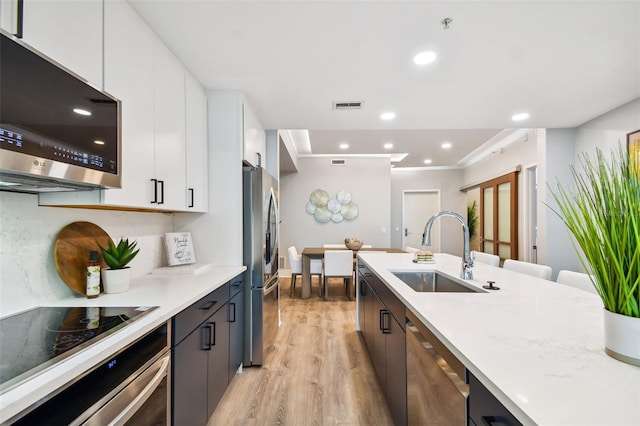 kitchen with appliances with stainless steel finishes, light hardwood / wood-style floors, white cabinetry, sink, and light stone countertops